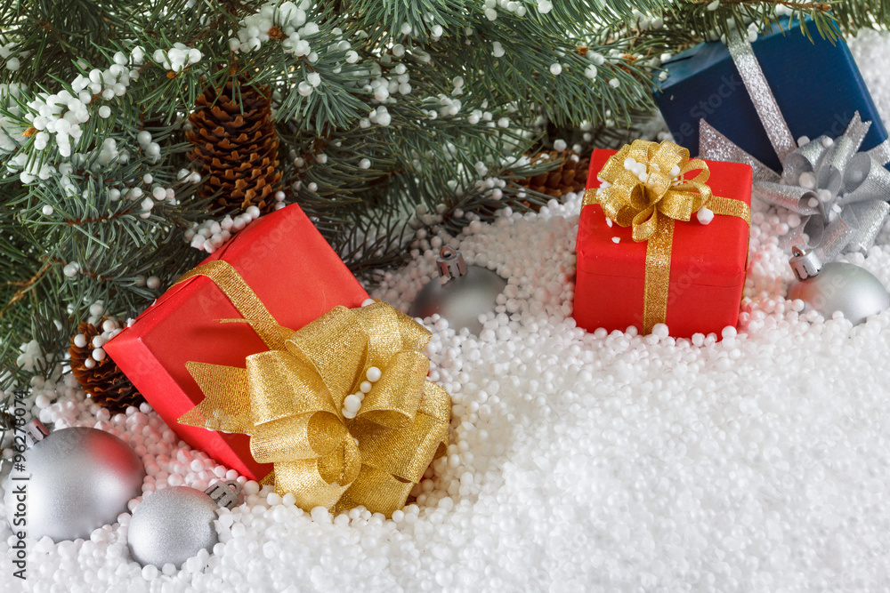 Red and blue boxes with gold ribbon in snow  under pine tree