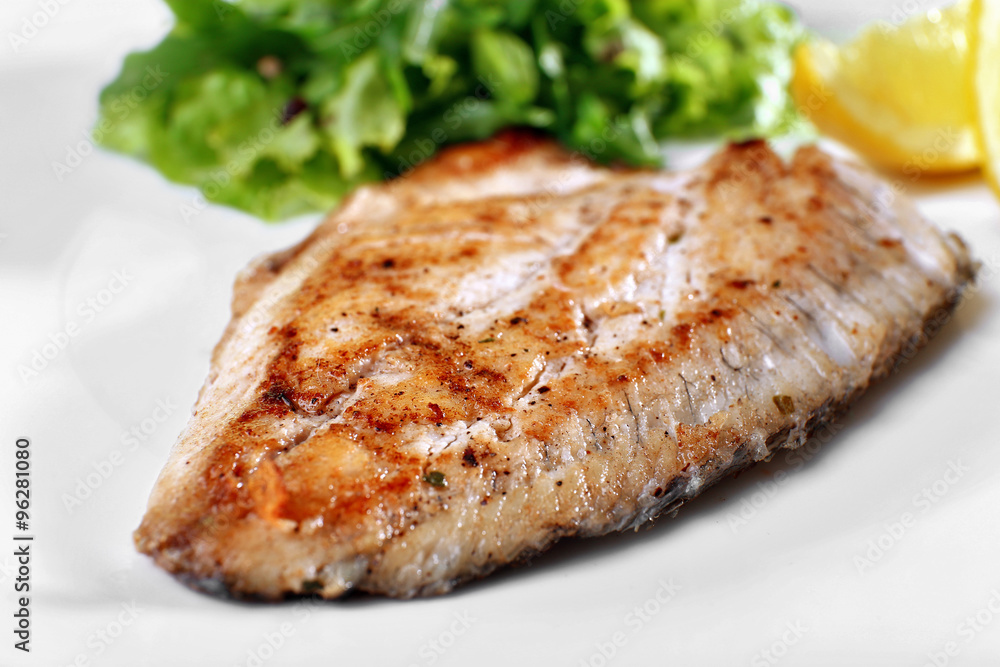 Dish of fish fillet with greens and lemon on plate close up Dish of fish fillet with greens and lemon on plate close up