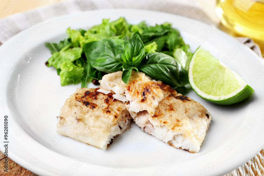 Dish of fish fillet with greens and lime on plate close up Dish of fish fillet with greens and lime on plate close up