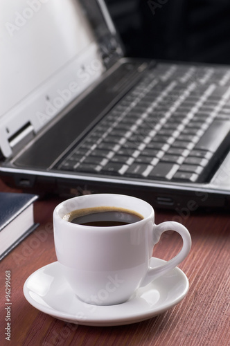 Desktop with coffee cup, opened laptop computer and diary on background, no people, focused on coffee