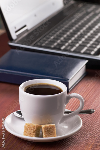 Desktop with coffee cup, opened laptop computer and diary, no people, focused on coffee