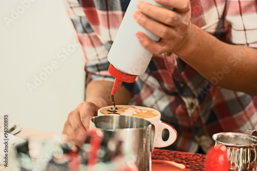 Cappuchino preparing. Barista painting over milk foam in cup