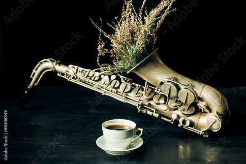 Photography Selective focus on cup of coffee with vintage saxophone and dry field flowers