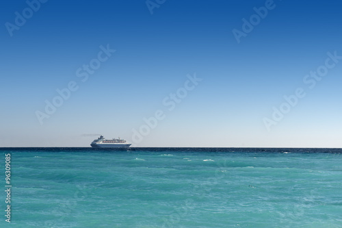 cruise liner sailing away on turquoise water and blue sky backround © ThomasLENNE