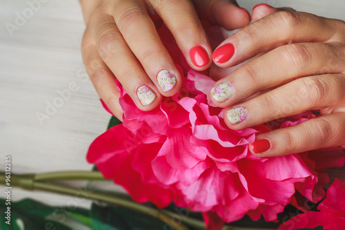 Red nail art with printed flowers on wooden background