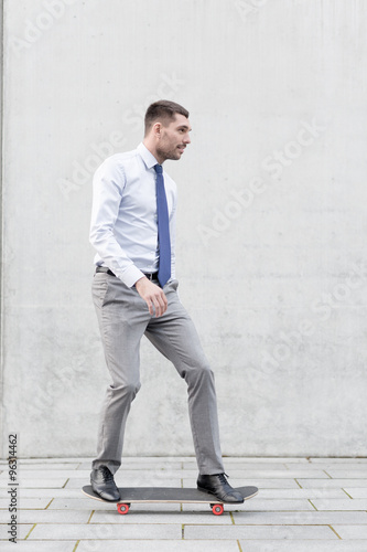 young smiling businessman with skateboard outdoors