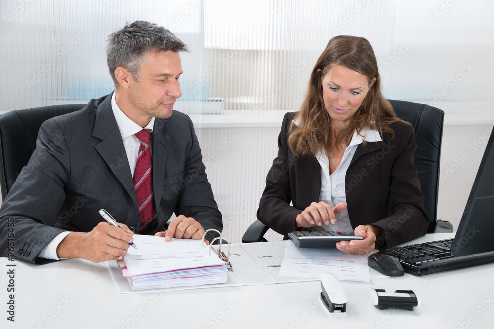 Two Businesspeople Calculating Tax In Office Two Businesspeople Calculating Tax In Office