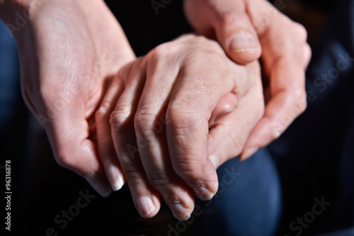 Young Woman Holding Old Woman's Hand Against Black Background