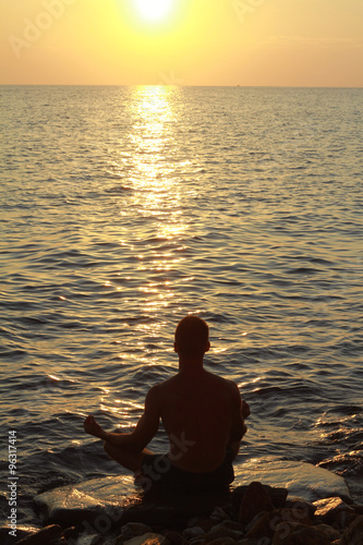 Close up on man meditating in yoga position on the beach near the sea at sunset