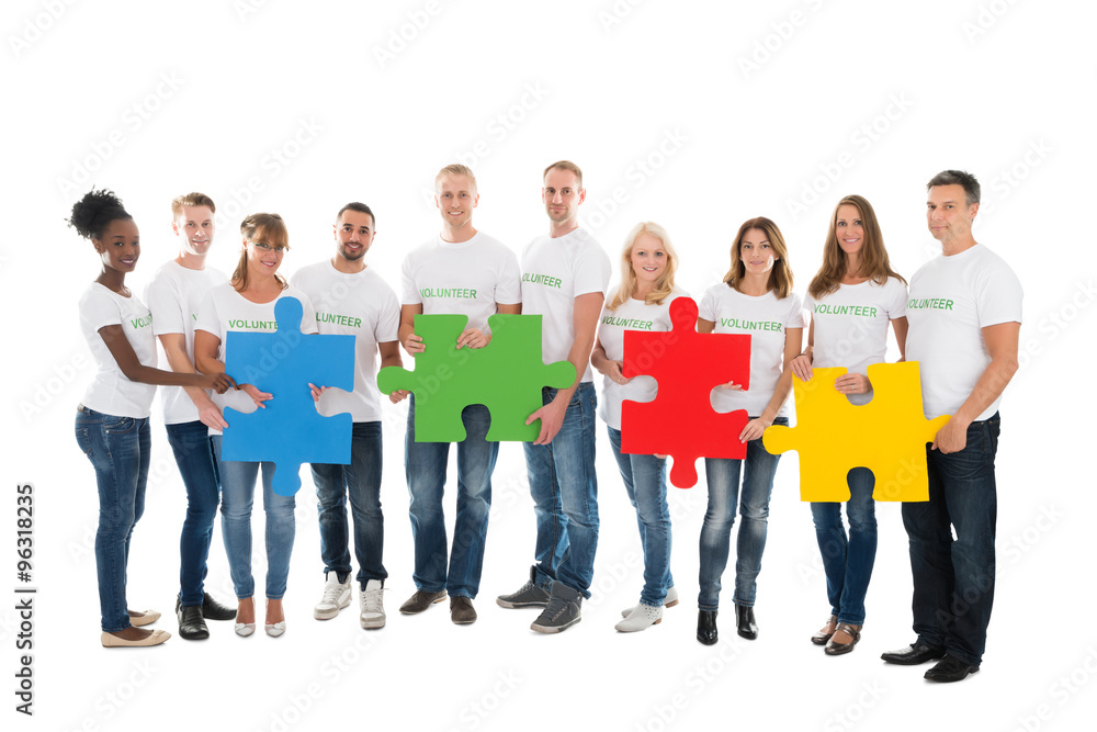 Portrait Of Confident Volunteers Holding Jigsaw Pieces Portrait Of Confident Volunteers Holding Jigsaw Pieces