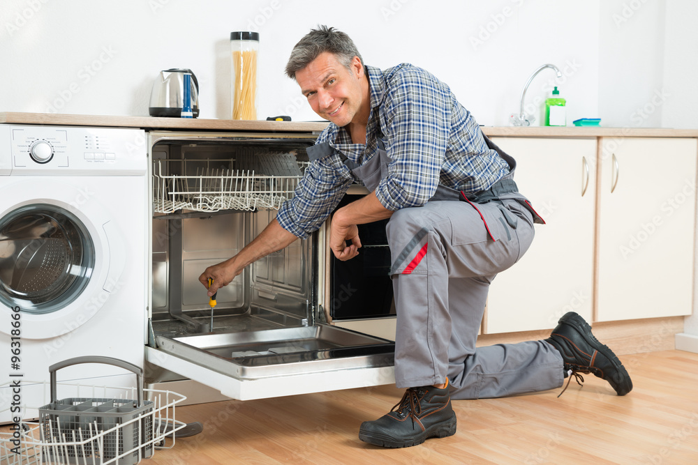 Repairman Repairing Dishwasher With Screwdriver In Kitchen Repairman Repairing Dishwasher With Screwdriver In Kitchen