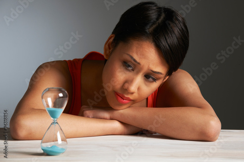 Sad Young Woman Looking At Hourglass photo