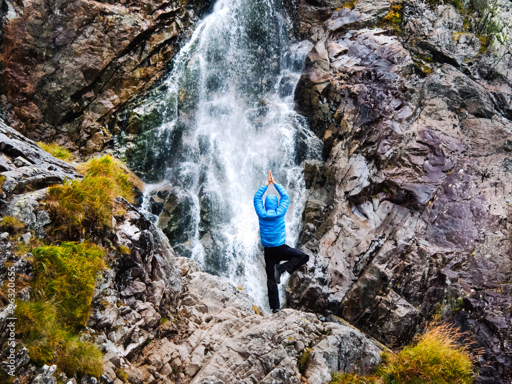 Young man in a yoga pose at the waterfall.
