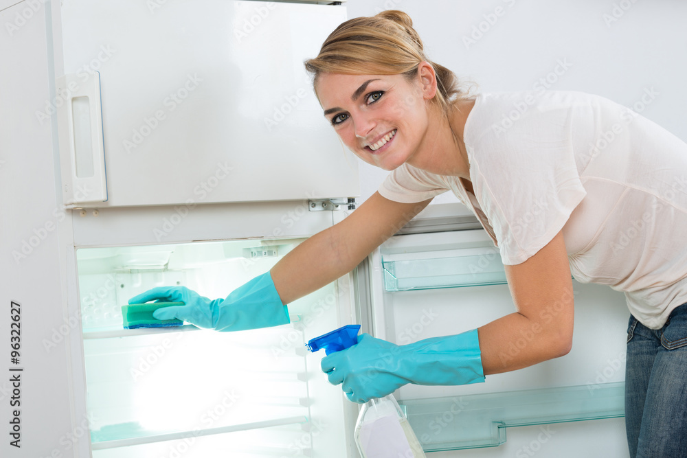 Smiling Woman Cleaning Refrigerator With Sponge And Spray Smiling Woman Cleaning Refrigerator With Sponge And Spray