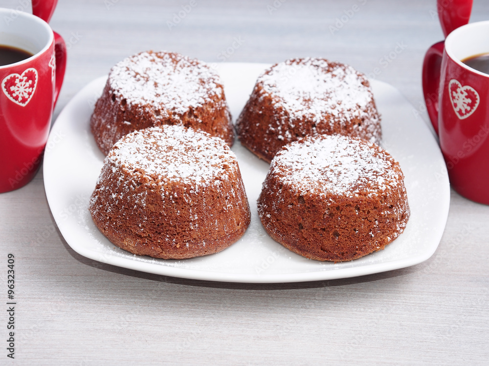 Chocolate muffins with iced sugar on a wooden table with red coffee cups with winter design Chocolate muffins with iced sugar on a wooden table with red coffee cups with winter design