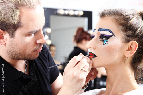makeup artist applying lipstick on model lips with brush photo