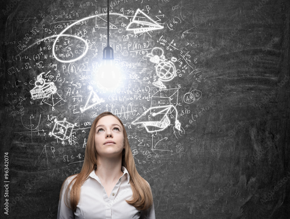 A beautiful lady is dreaming about graduation. Math formulas, an arrow and geometric figures are drawn on the black chalkboard. A light bulb as a concept of idea. A beautiful lady is dreaming about graduation. Math formulas, an arrow and geometric figures are drawn on the black chalkboard. A light bulb as a concept of idea.