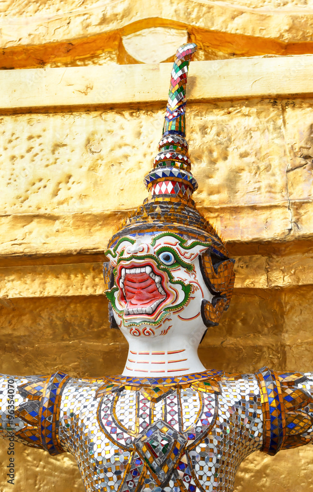 Focus head of white Thai giant demon Yaksha statue with gold chedi at Wat Phra Kaew, Bangkok Thailand.