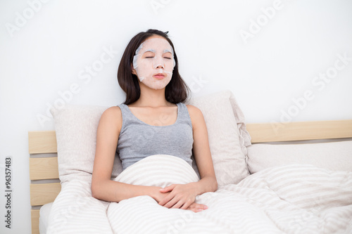 Asian woman use of the facial mask and sitting in bed