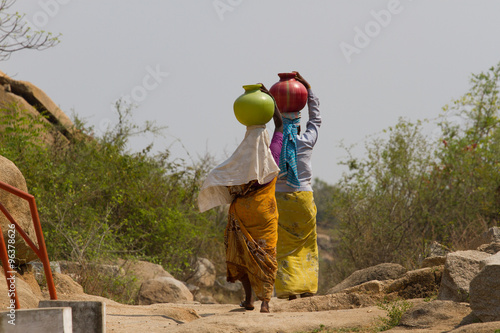 Two Indian women carry water on their heads in  pots 