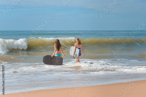Back view of beautiful young women with surfboards entering sea