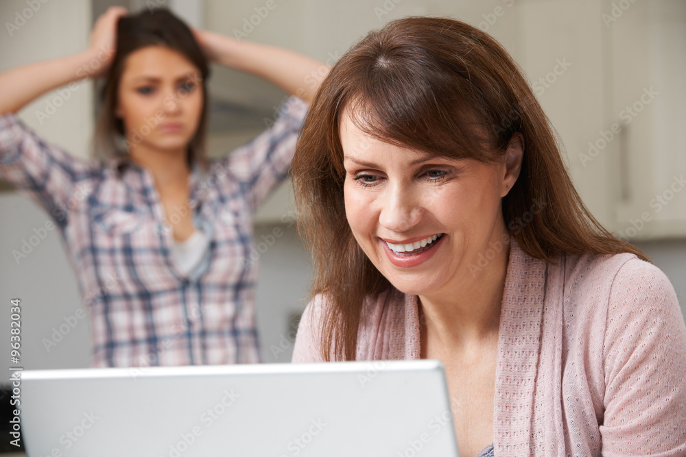Mother Using Laptop With Frustrated Daughter In Background Mother Using Laptop With Frustrated Daughter In Background