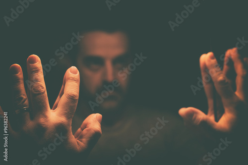 Man in despair with raised hands, in a low light room looking at his reflection in a mirror