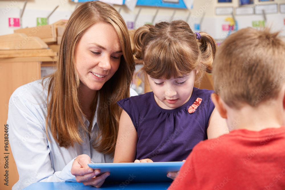 Teacher Helping Elementary School Pupil Use Digital Tablet Teacher Helping Elementary School Pupil Use Digital Tablet