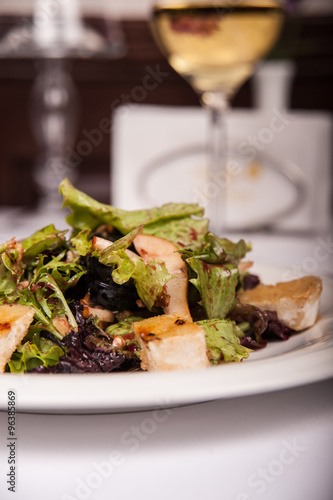 Salad with meat and lettuce on a plate in a restaurant, a glass of white wine