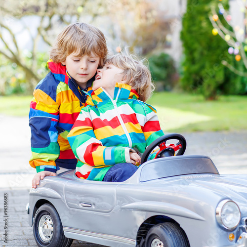 Two happy sibling boys playing with big old toy car 