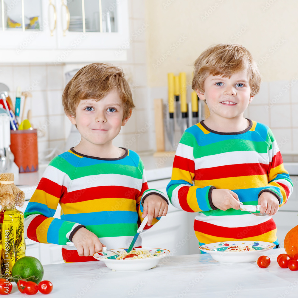 Fototapeta premium Two little kid boys eating spaghetti in domestic kitchen.