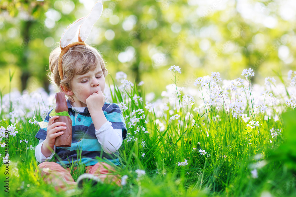 Cute happy little boy wearing Easter bunny ears and eating choco Cute happy little boy wearing Easter bunny ears and eating choco