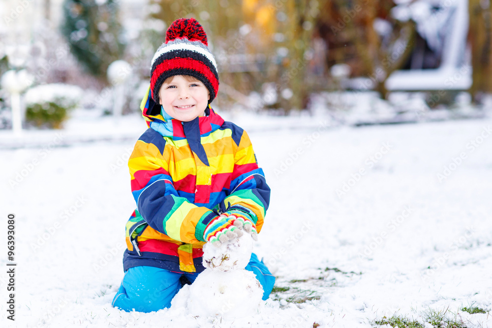 Beautiful kid boy in colorful clothes making a snowman