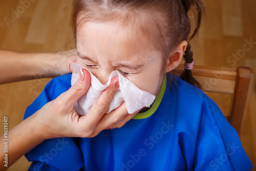 Parent hand helping the playing little girl to blow her nose with a hygienic wet wipe. Seasonal sickness.