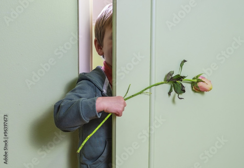 cute child hiding behind the door with a flower