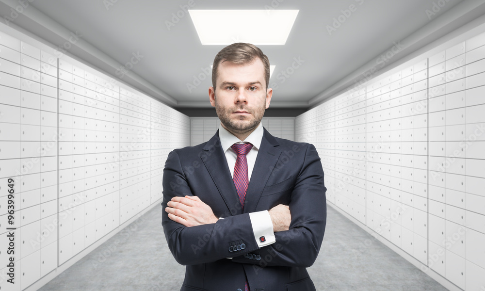 A private manger of a bank with crossed hands is standing in a room with safe deposit boxes. A concept of storing of important documents or valuables in a safe and secure environment. A private manger of a bank with crossed hands is standing in a room with safe deposit boxes. A concept of storing of important documents or valuables in a safe and secure environment.