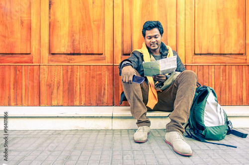 Young indian guy looking city map holding mobile phone - Asian model male next to old wooden door - Cheerful afro american student reading - Concept of tourism DIY and freedom - Soft vintage filter
