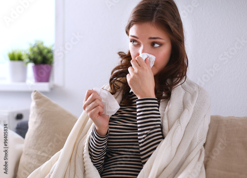 Portrait of a sick woman blowing her nose while sitting on the sofa photo