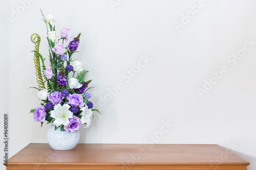 Artificial flower vase on wooden table and white wall
