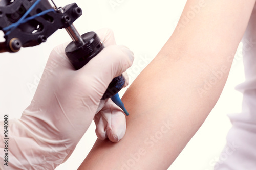 Tattooist draws on the woman's arm on white background, close up