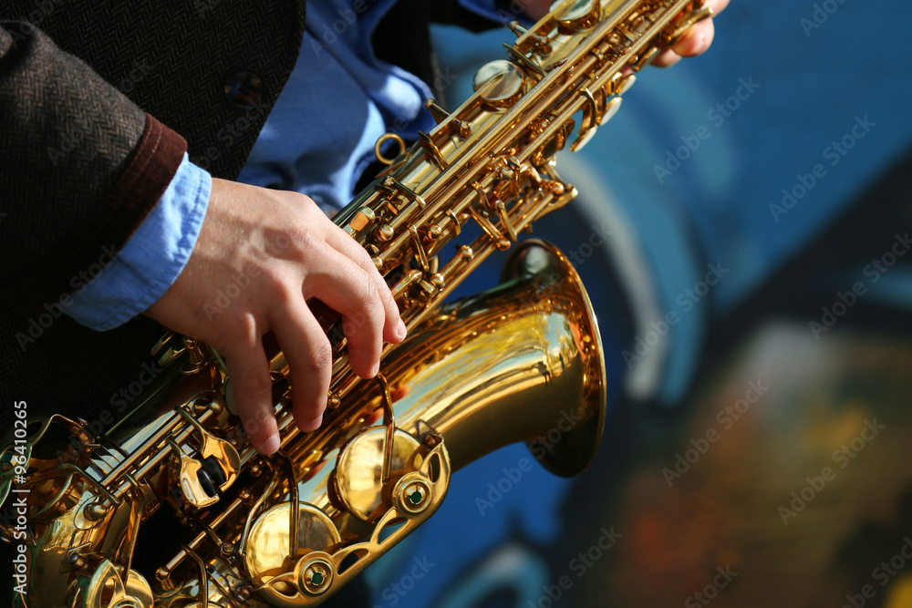 Fototapeta premium Young man with saxophone outside near the old painted wall