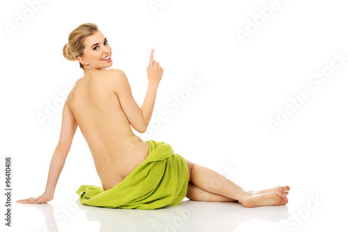 Young happy woman after bath or spa sitting on the floor wrapped in towel and show somenthing