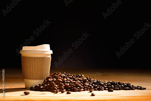 Paper cup of coffee and coffee beans on wooden table