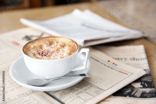 Cup of tasty cappuccino and newspapers on table