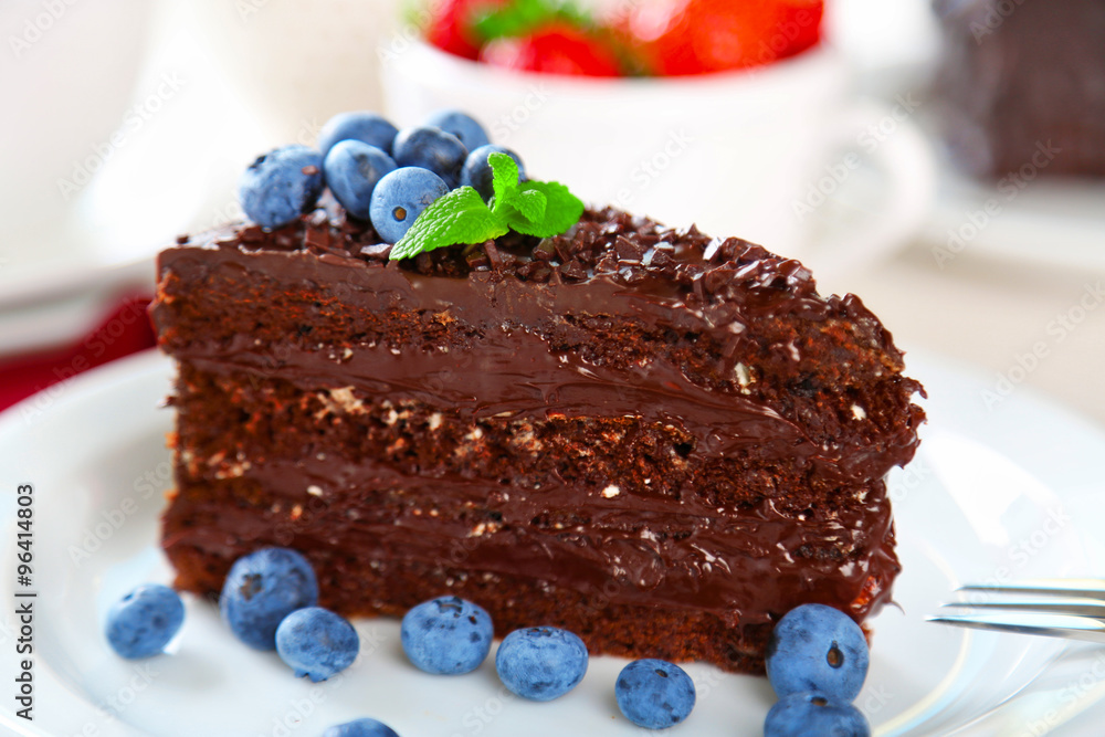 Chocolate cake with chocolate cream and fresh berries on plate, on wooden table, on light background Chocolate cake with chocolate cream and fresh berries on plate, on wooden table, on light background