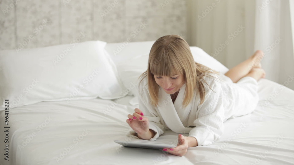 Young woman lying on bed and using touchpad Young woman lying on bed and using touchpad