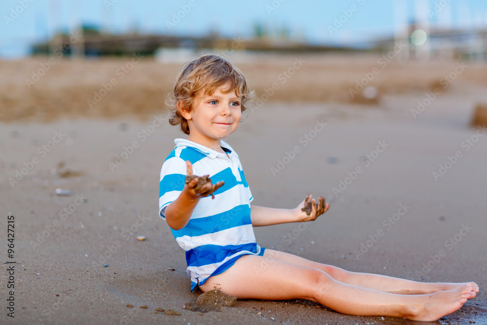 Happy little kid boy having fun with sand castle by ocean Happy little kid boy having fun with sand castle by ocean