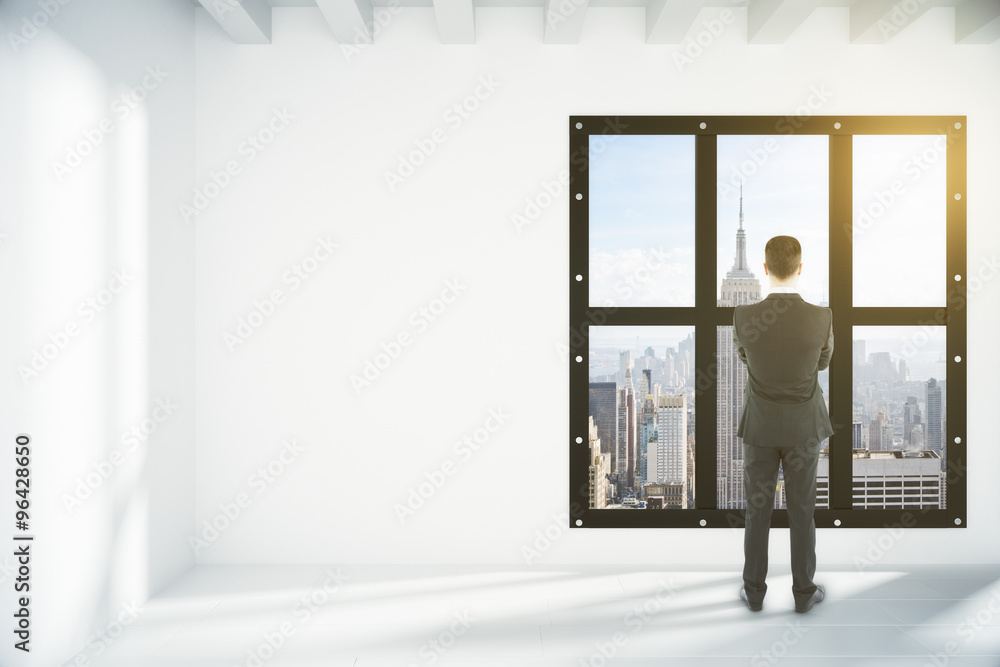 Fototapeta premium Businessman in white empty loft room with megapolis city view