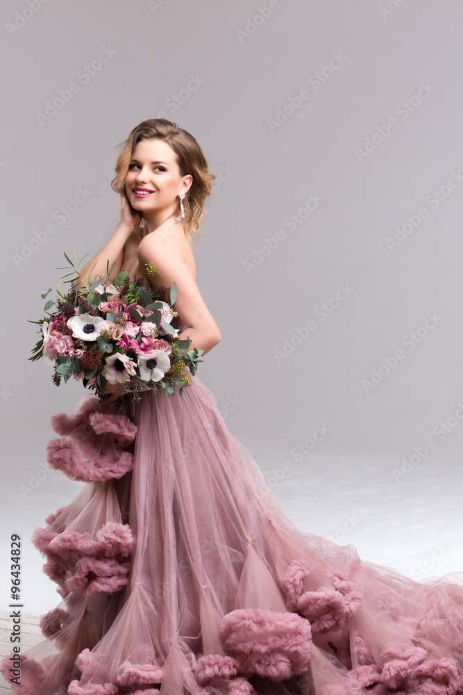 Portrait of a beautiful woman with a bouquet in a long pink dress.