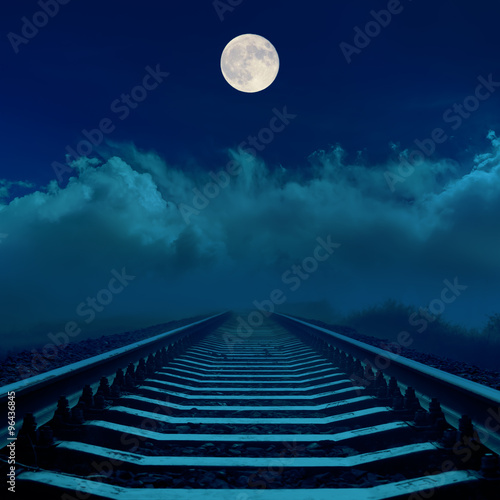 full moon in dark sky over railroad and clouds